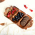 Wooden charcuterie board with compartments filled with fruits and cookies on a white surface.